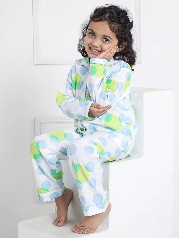 Child wearing a patterned onesie sitting on a white stool.